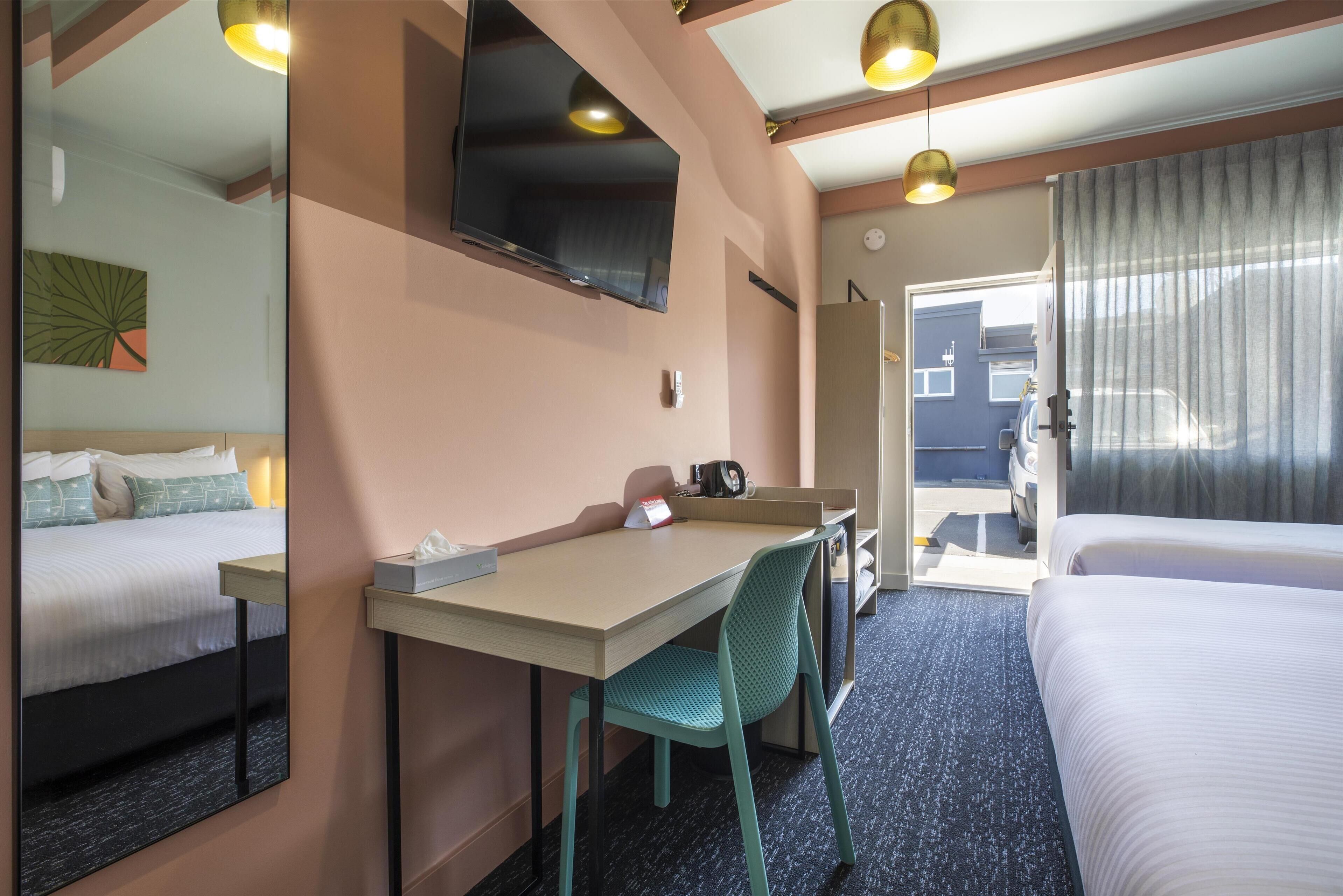 Een hotelkamer met een bed, een bureau met stoel, een televisie en een deur die leidt naar een balkon.