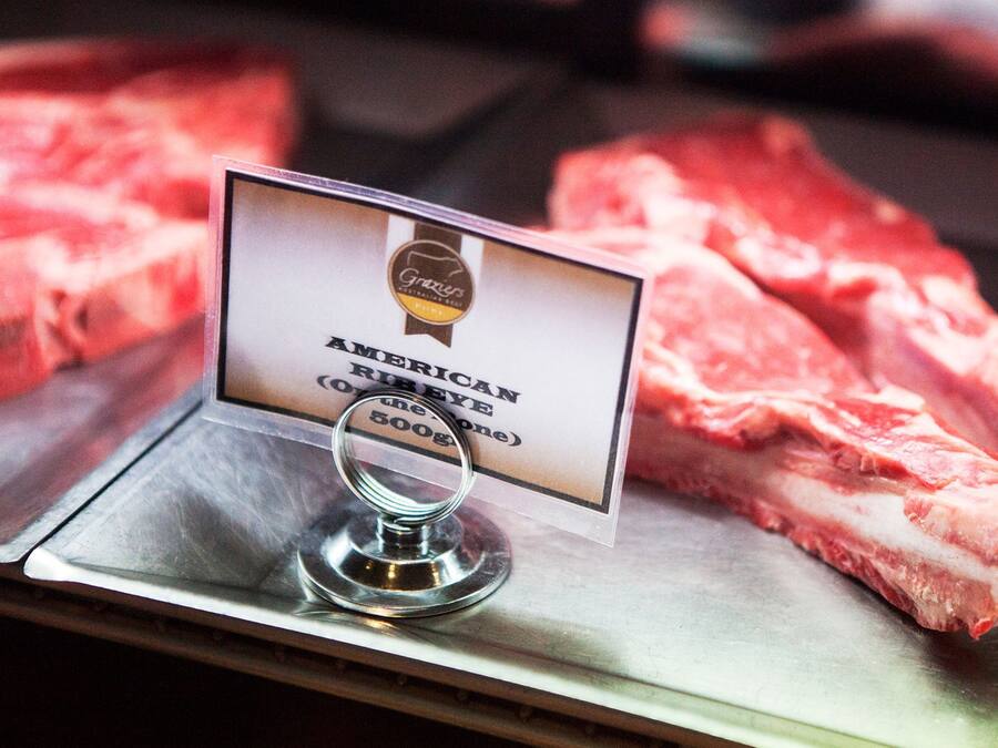 A sign indicating American Prime Rib Eye (500g) on a display with raw meat.