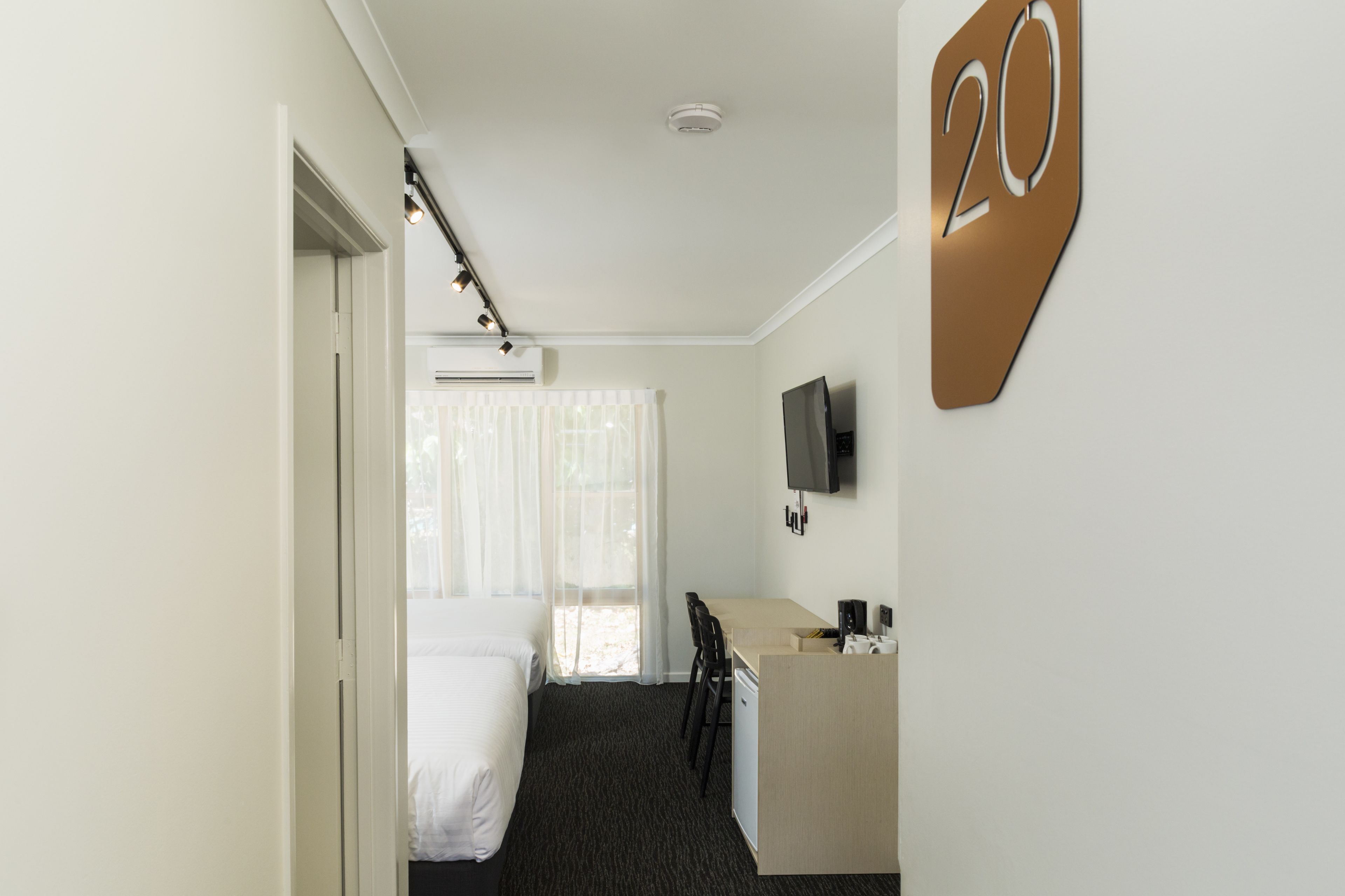 Hotelkamer met een bed, bureau, stoel, televisie en nummerbord met daarop kamer 20.