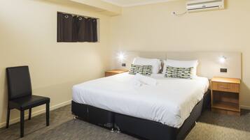A neatly arranged hotel room with a large bed, bedside tables, a chair, and an air conditioning unit on the wall.