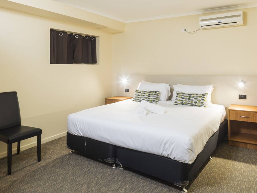 A neatly arranged hotel room with a large bed, bedside tables, a chair, and an air conditioning unit on the wall.