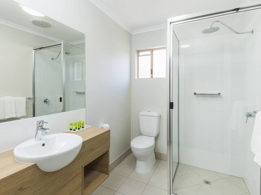 A modern bathroom with a white sink, wooden vanity, a toilet, and a glass-enclosed shower.