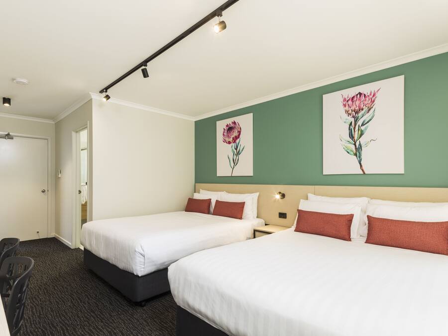 Habitación de hotel con dos camas, un escritorio y una silla. Se observan dos cuadros en la pared, una puerta y una ventana.