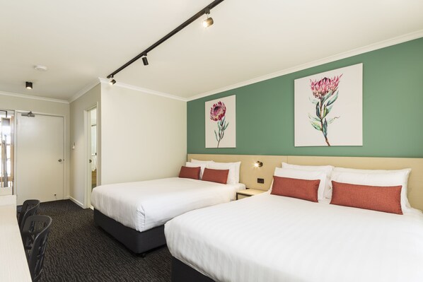 Habitación de hotel con dos camas, un escritorio y una silla. Se observan dos cuadros en la pared, una puerta y una ventana.