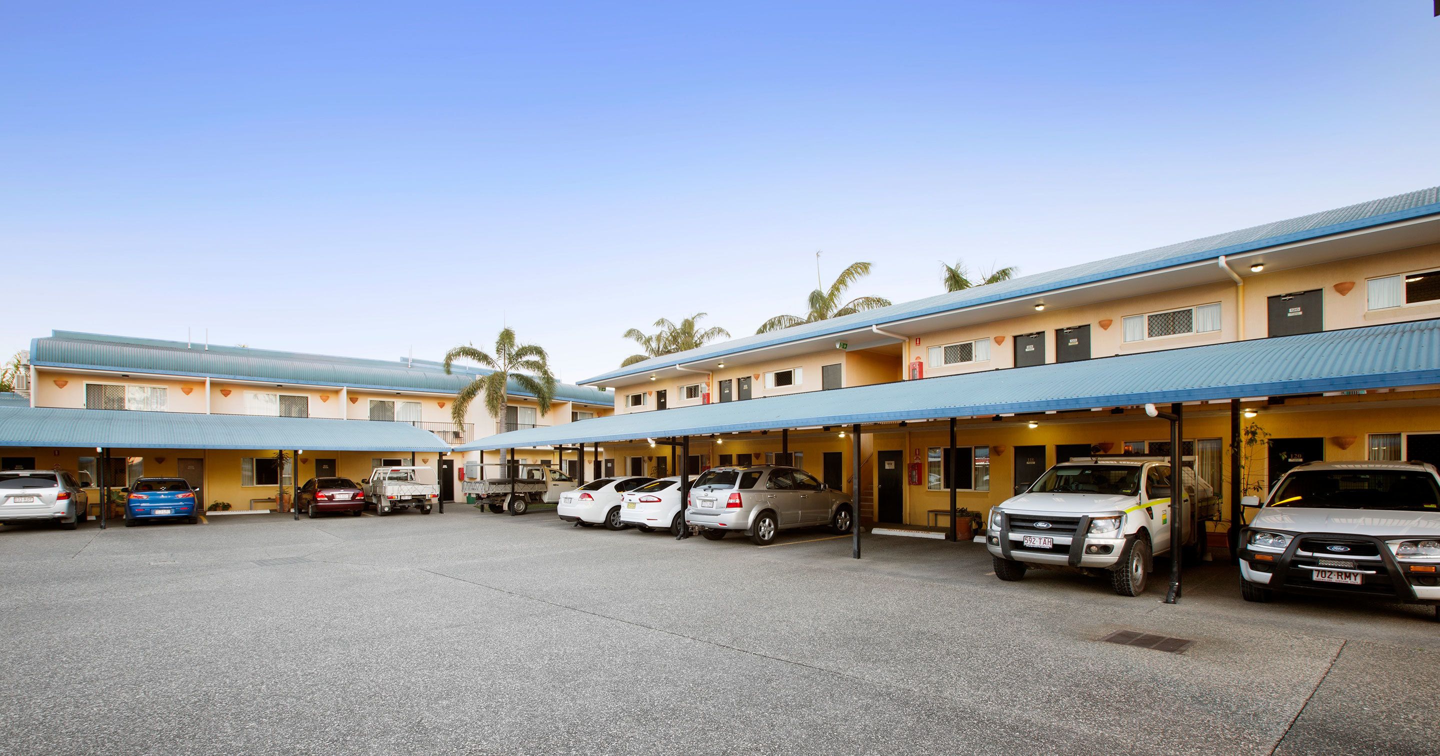 Ein Motel mit mehreren Parkplätzen, einem überdachten Parkbereich und einem Gebäude mit blauem Dach.