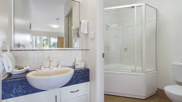 Un baño con lavamanos blanco, encimera de mármol y ducha con mampara de vidrio.