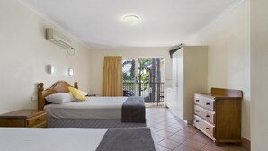 A hotel room with two beds, a dresser, and a balcony with a view of palm trees. - Glenmore Tavern (Norman Gardens)