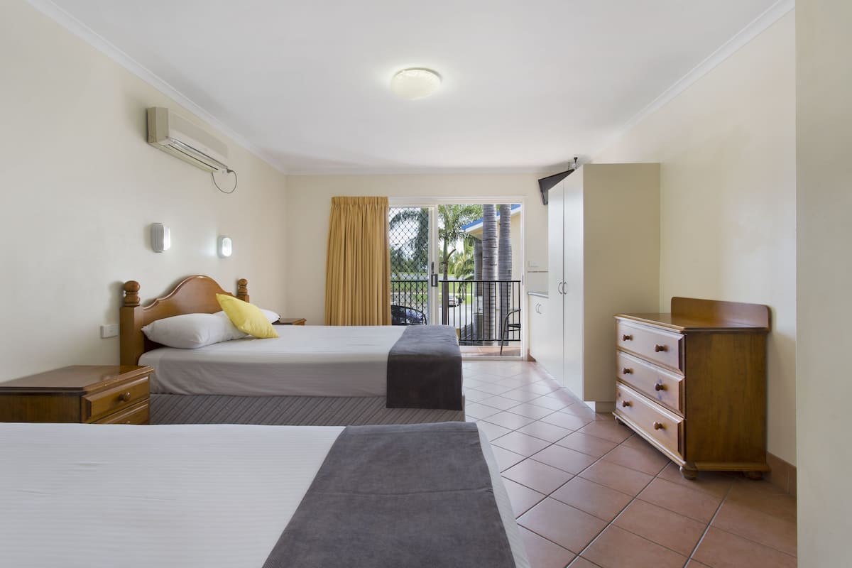 A hotel room with two beds, a dresser, and a balcony with a view of palm trees.