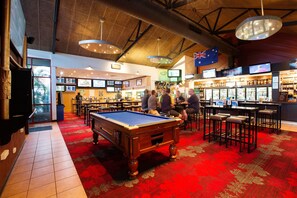 A pool table in a room with a red carpet, bar area with stools, and a flag.