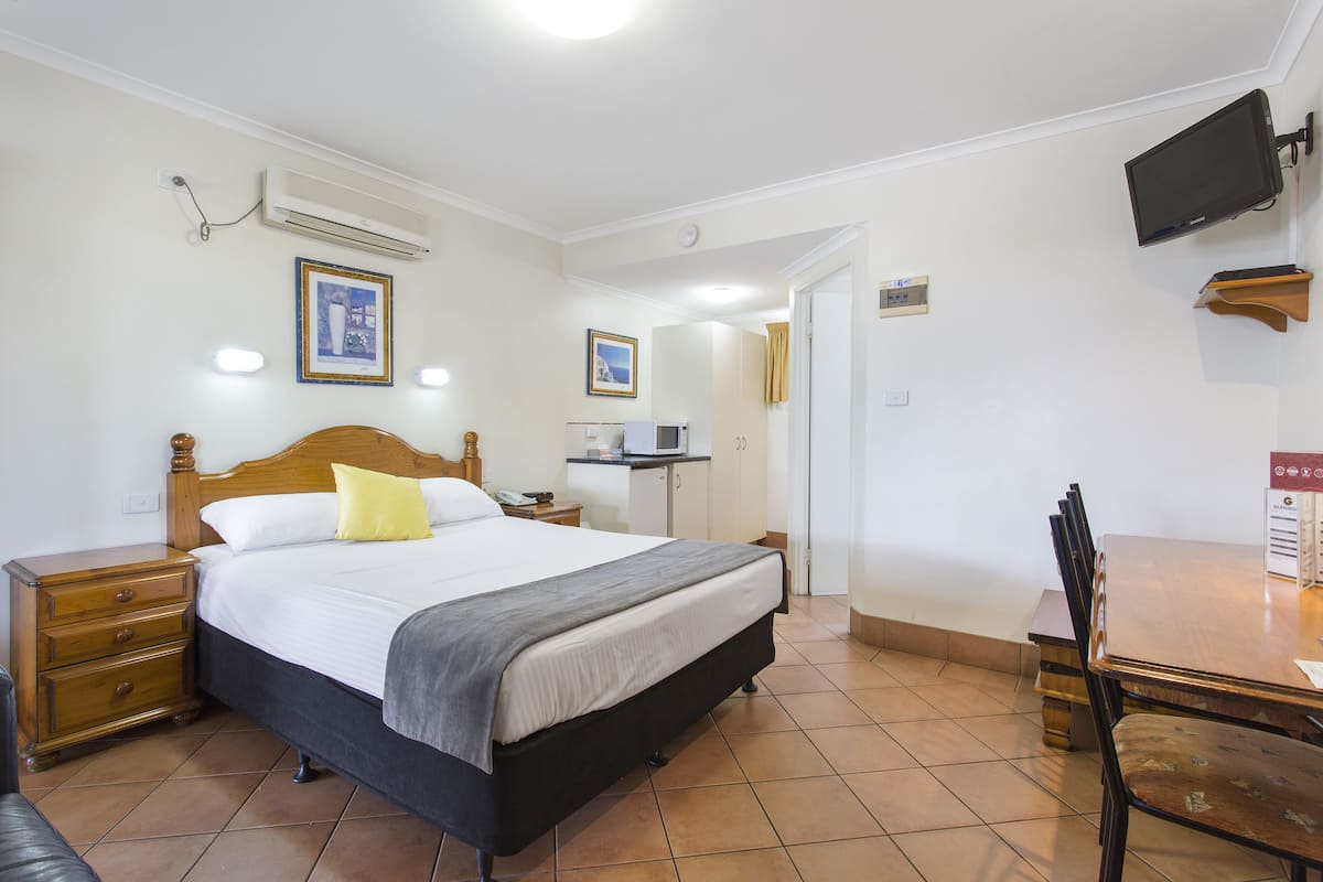 A hotel room with a bed, bedside table, lamp, and a TV mounted on the wall.