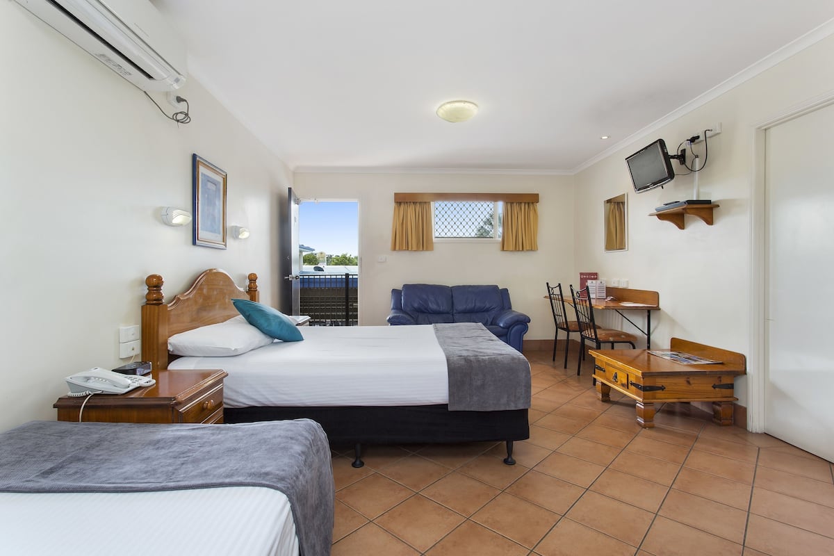 A hotel room with a bed, a desk, a chair, a TV, and an air conditioning unit.