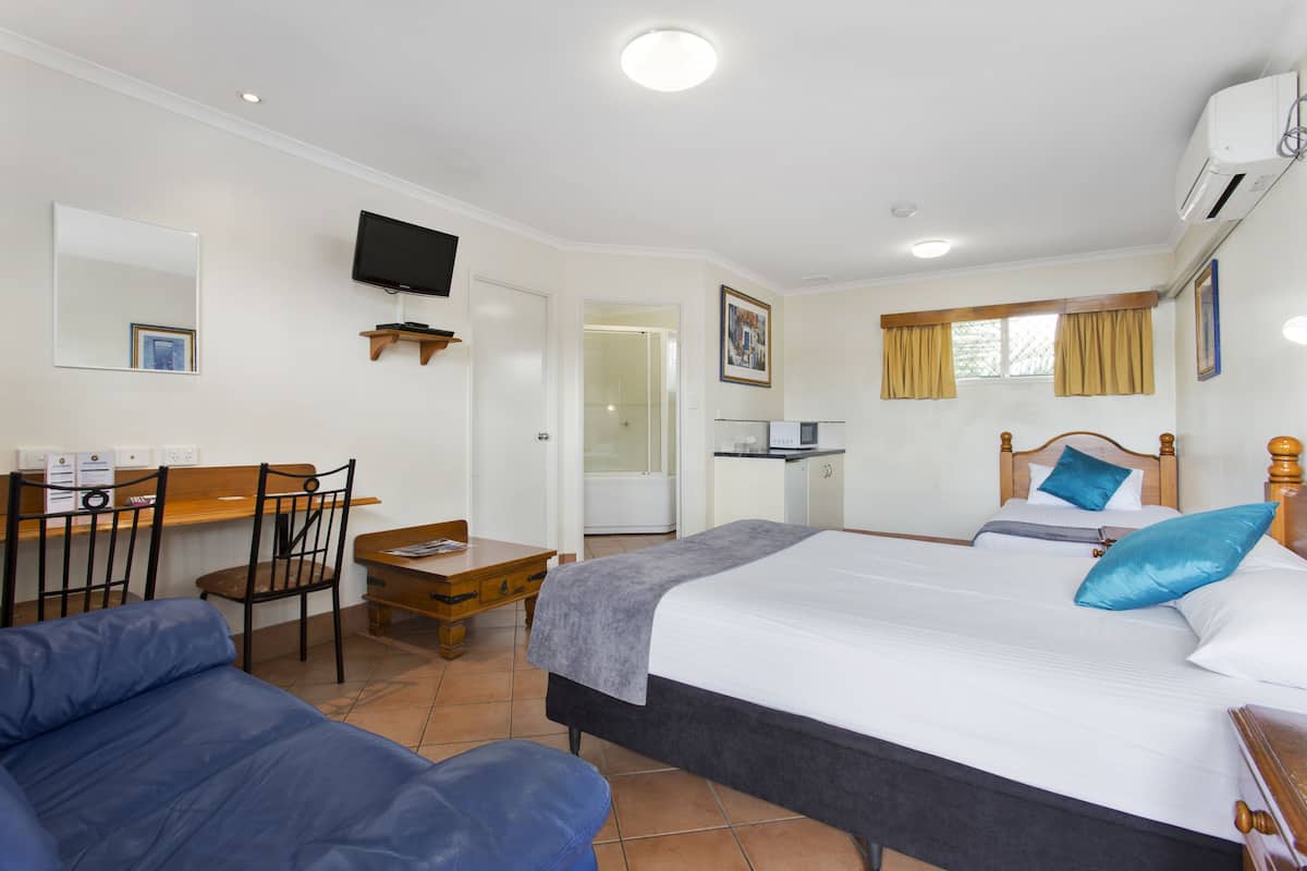 A hotel room with a bed, a desk, a chair, a sofa, and a TV.