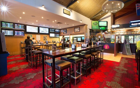 A bar area with multiple screens displaying sports content, a bar counter, and stools.