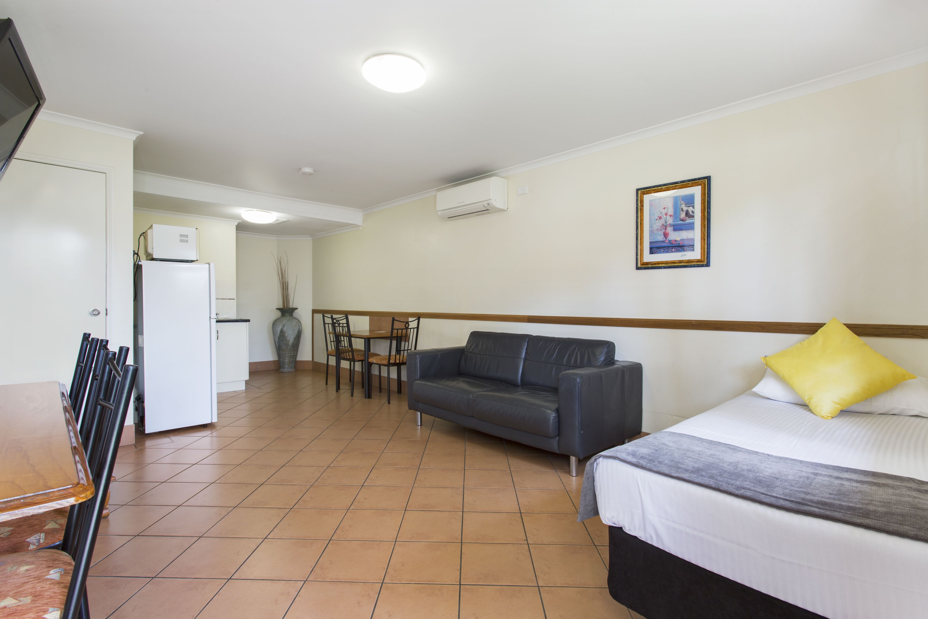 Una habitación de hotel con cama, sofá, mesa de comedor con sillas, una pequeña kitchenette y televisión.