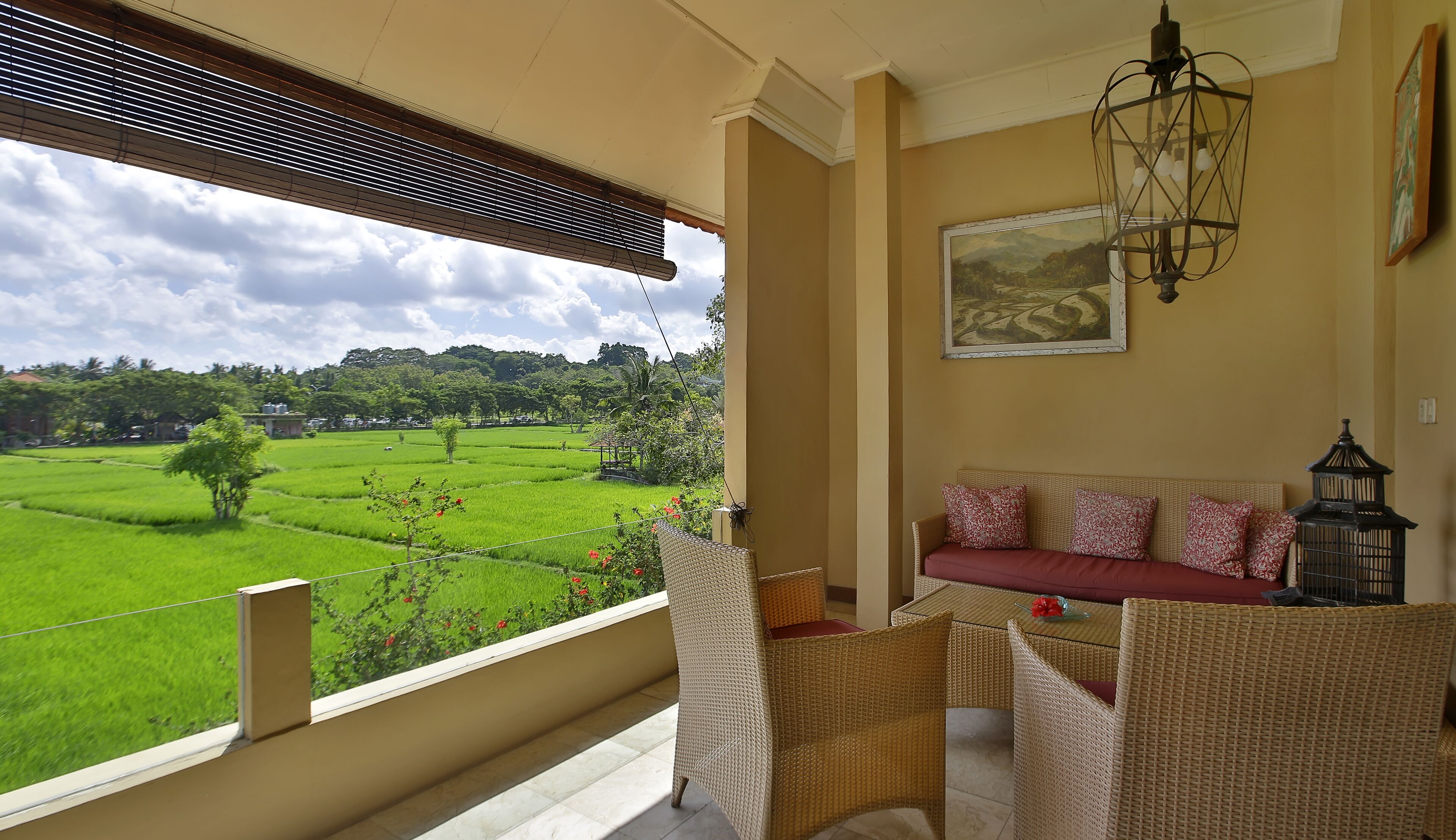 A balcony with wicker furniture, a view of green fields, and a painting on the wall.