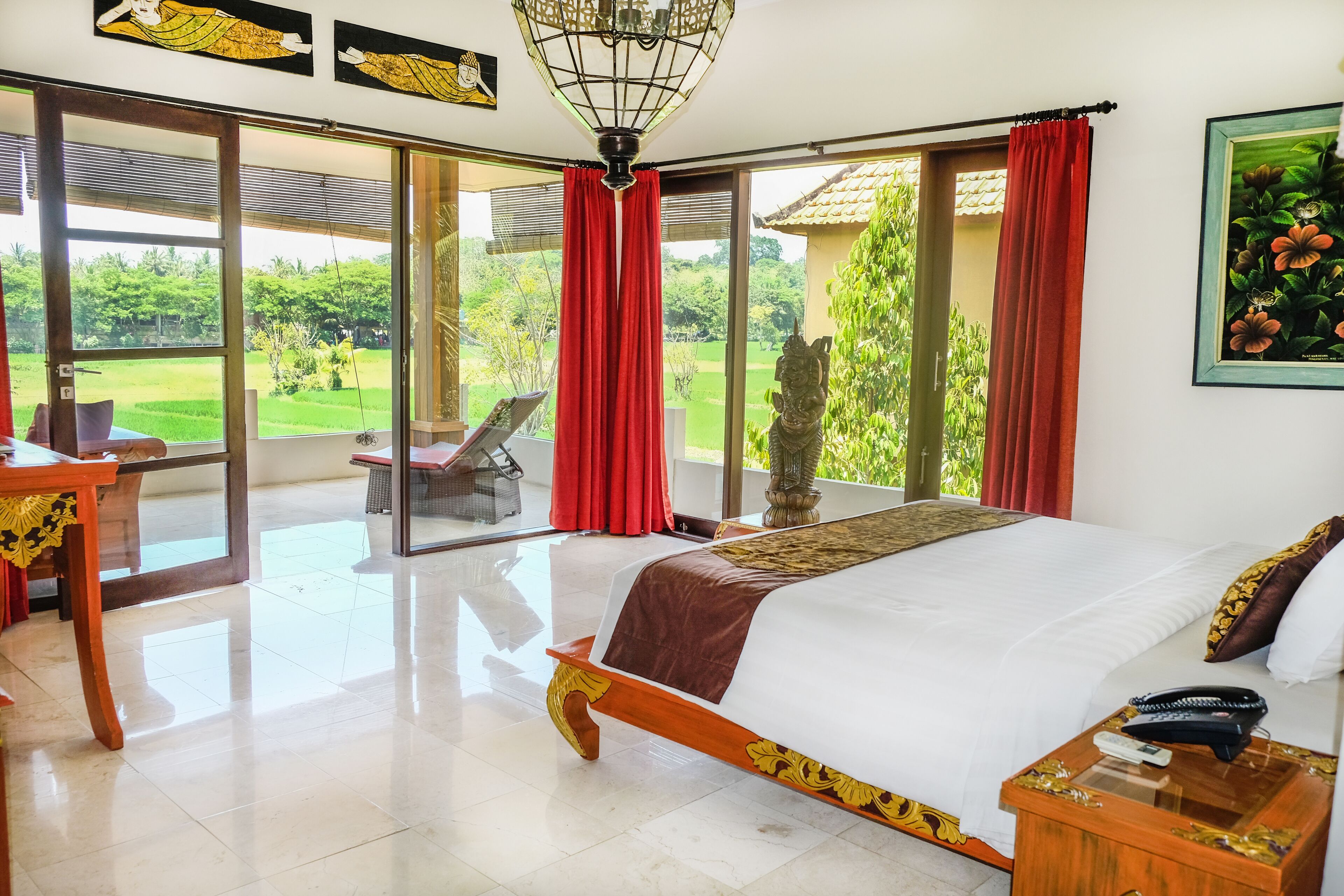 Un dormitorio amplio con una cama grande, una mesita de noche de madera y vistas a un jardín exuberante a través de puertas correderas de vidrio.