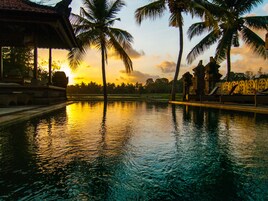 A swimming pool with palm trees and a sunset in the background.
