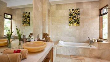A bathroom with a large bathtub, a round sink, and a mirror. There are towels and toiletries on the counter.