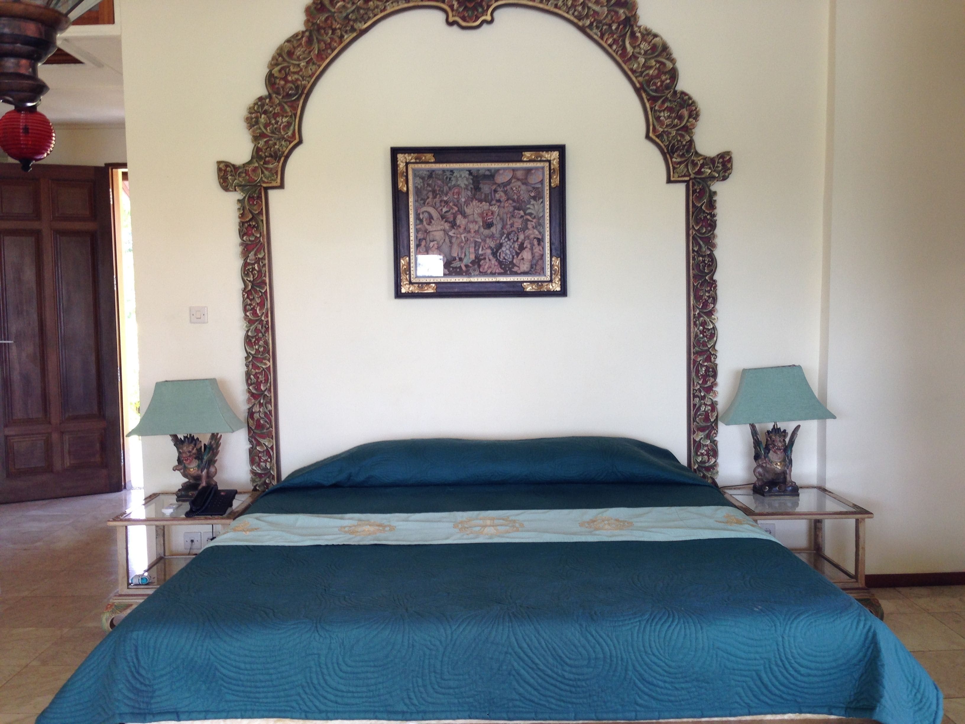 A bedroom with a large bed, ornate headboard, two bedside tables with lamps, and a framed artwork above the bed.