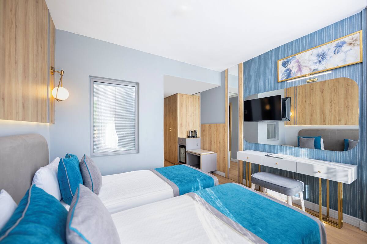 A modern hotel room with two beds, a desk, a TV, and a bathroom.
