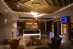 A hotel reception area with a modern design, including a reception desk, seating area, and a television screen displaying a news channel. - Sealife Lounge Hotel - Adult Only (Konyaalti)