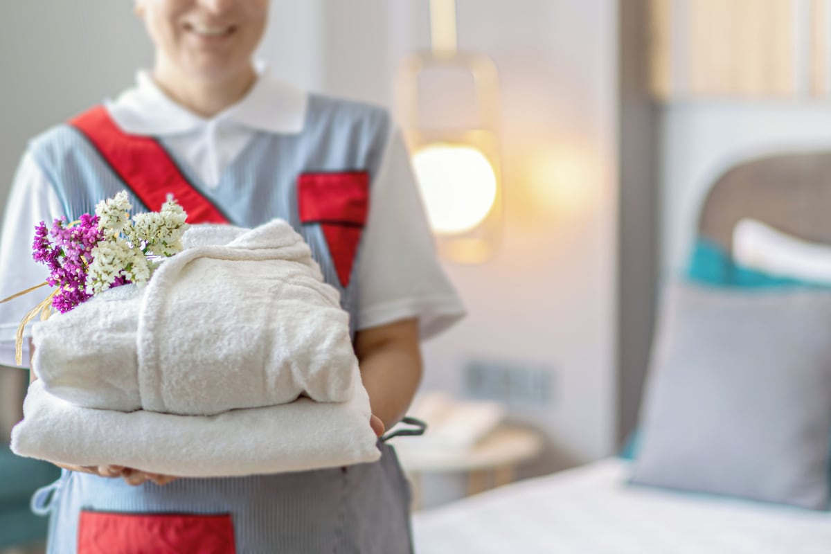 Una persona sostiene una pila de toallas blancas y un ramo de flores, probablemente un miembro del personal de un hotel.