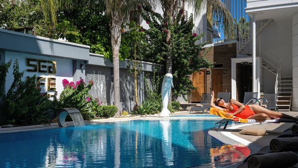 A swimming pool with a water feature, surrounded by greenery and a building with a sign that reads "SEA".