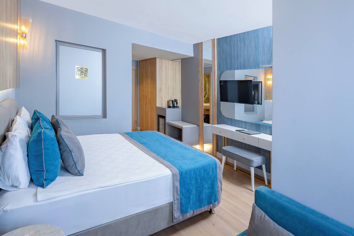 A modern hotel room with a bed, a desk, a chair, and a television.