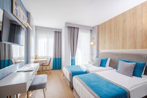 Quarto de hotel com duas camas, uma escrivaninha, uma cadeira e uma televisão.