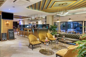 Un moderno vestíbulo de hotel con una zona de bar, arreglos de asientos y un amplio ventanal con vistas.