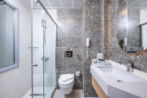 Uma casa de banho moderna com cabine de duche em vidro, sanita branca e uma grande pia com painel de fundo em mármore.