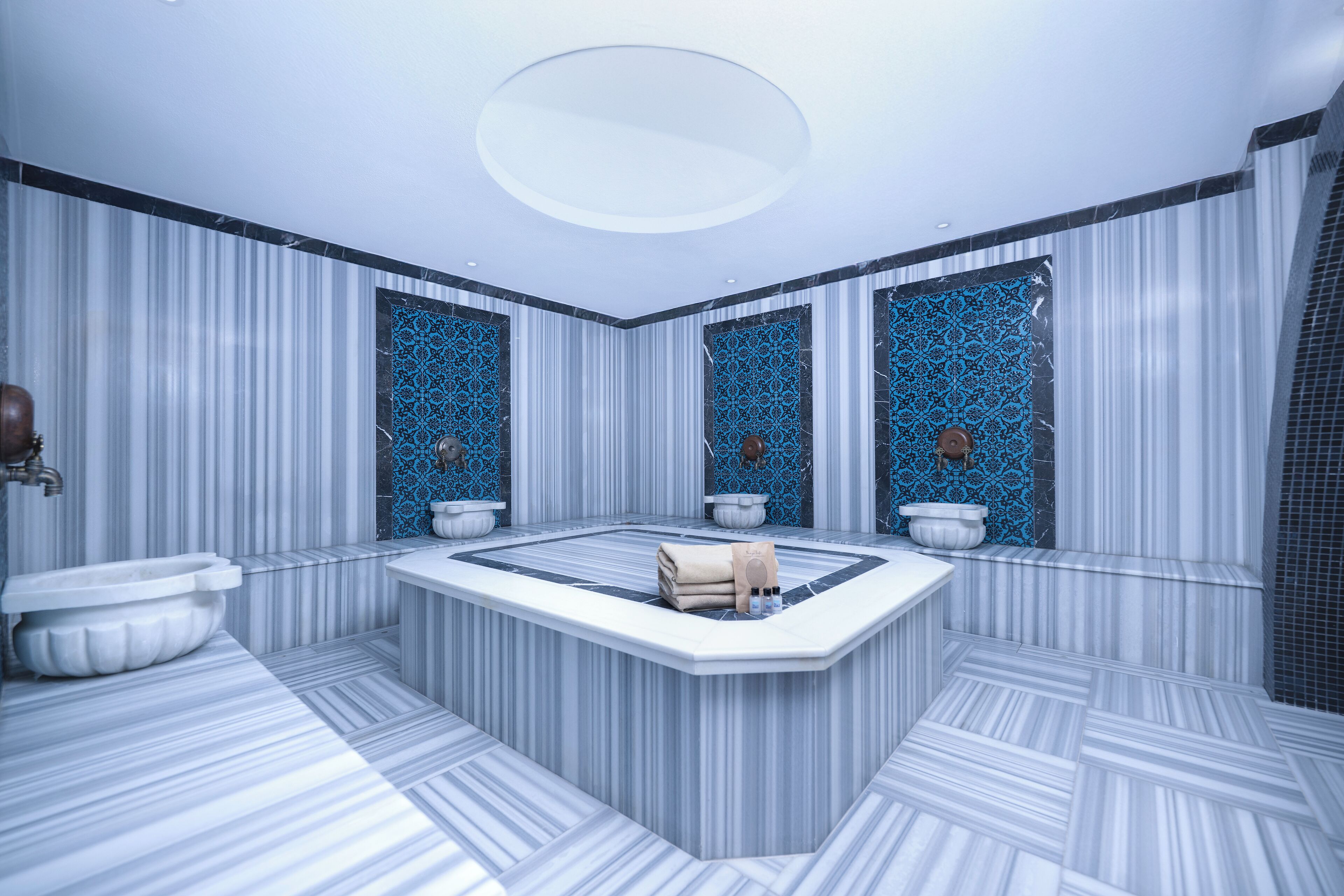 A modern bathroom with a central jacuzzi, striped marble walls, and decorative blue tiles.