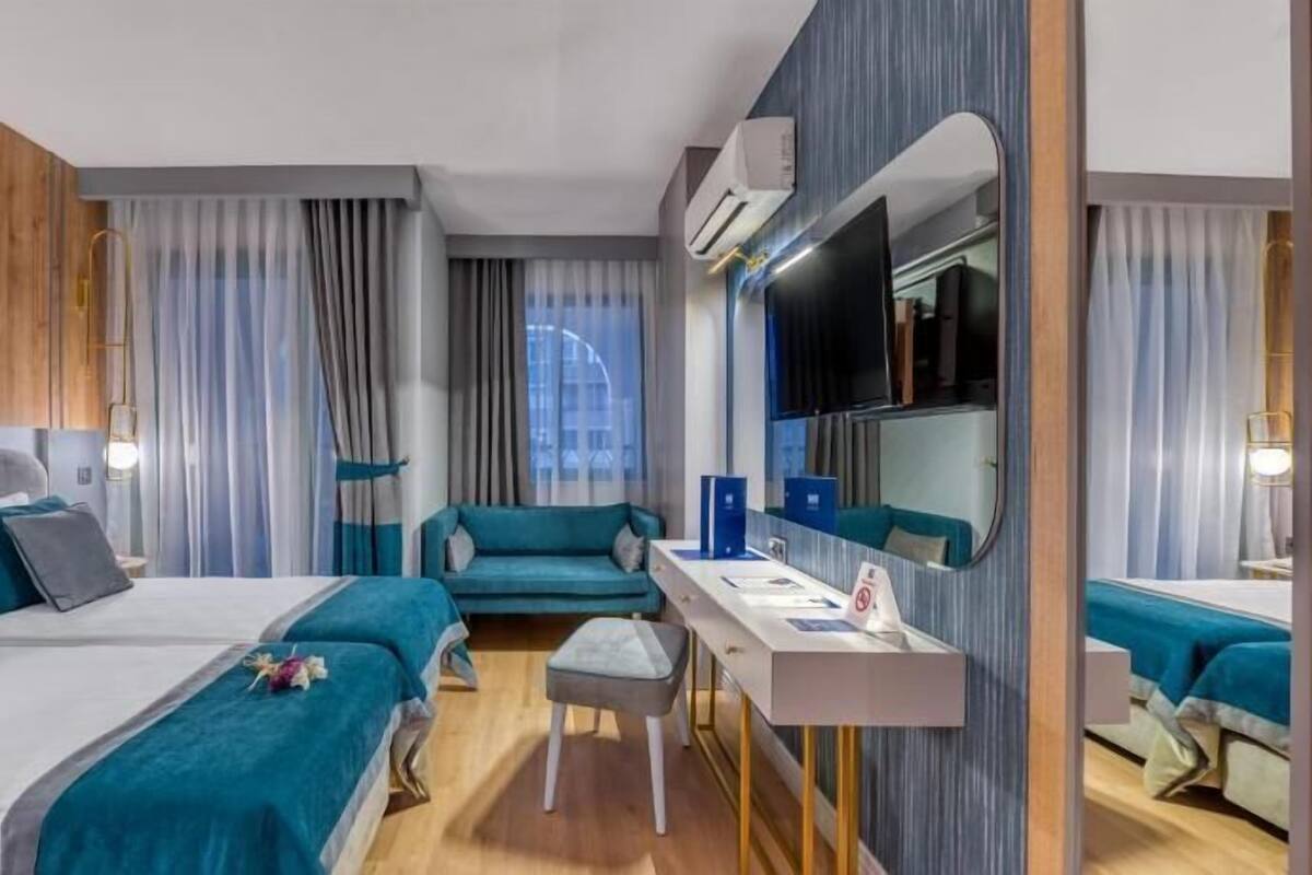 A hotel room with two beds, a desk, a chair, a mirror, and a view of the city.