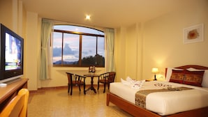 Habitación de hotel con cama, televisión, mesa con sillas, ventana con vistas y lámpara.