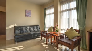 Una sala de estar con un sofá de cuero negro, una mesa de comedor de madera y sillas. Hay un cuadro en la pared y una ventana con cortinas.