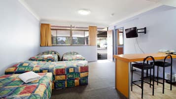 A hotel room with two beds, a desk with chairs, a TV, and a view of the street.