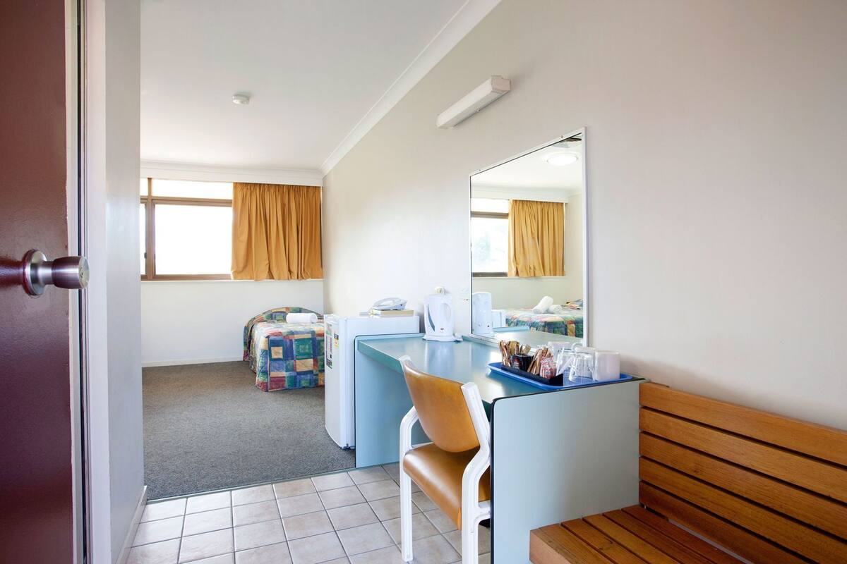 A hotel room with a bed, a desk, a chair, a mirror, and a window with curtains.