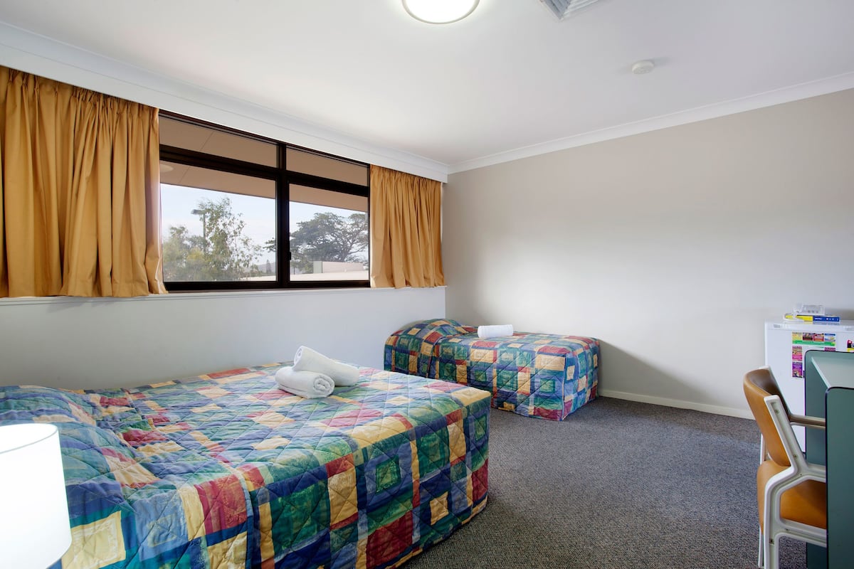 A room with two beds, a desk, and a window with curtains.