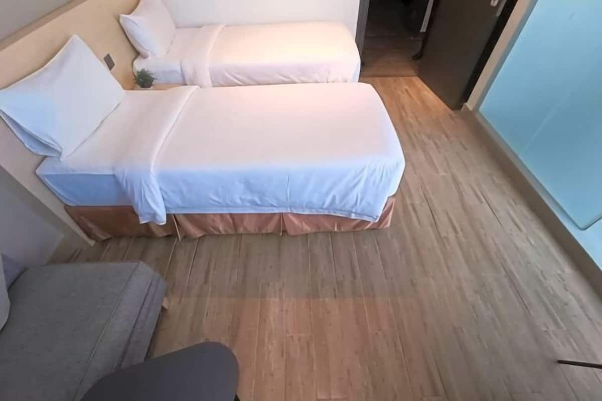 Una habitación con dos camas, piso de madera y un sofá gris.