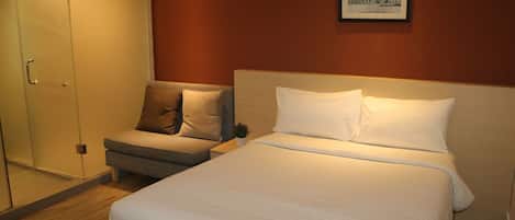 A hotel room with a bed, a sofa, a small table, and a glass door closet.