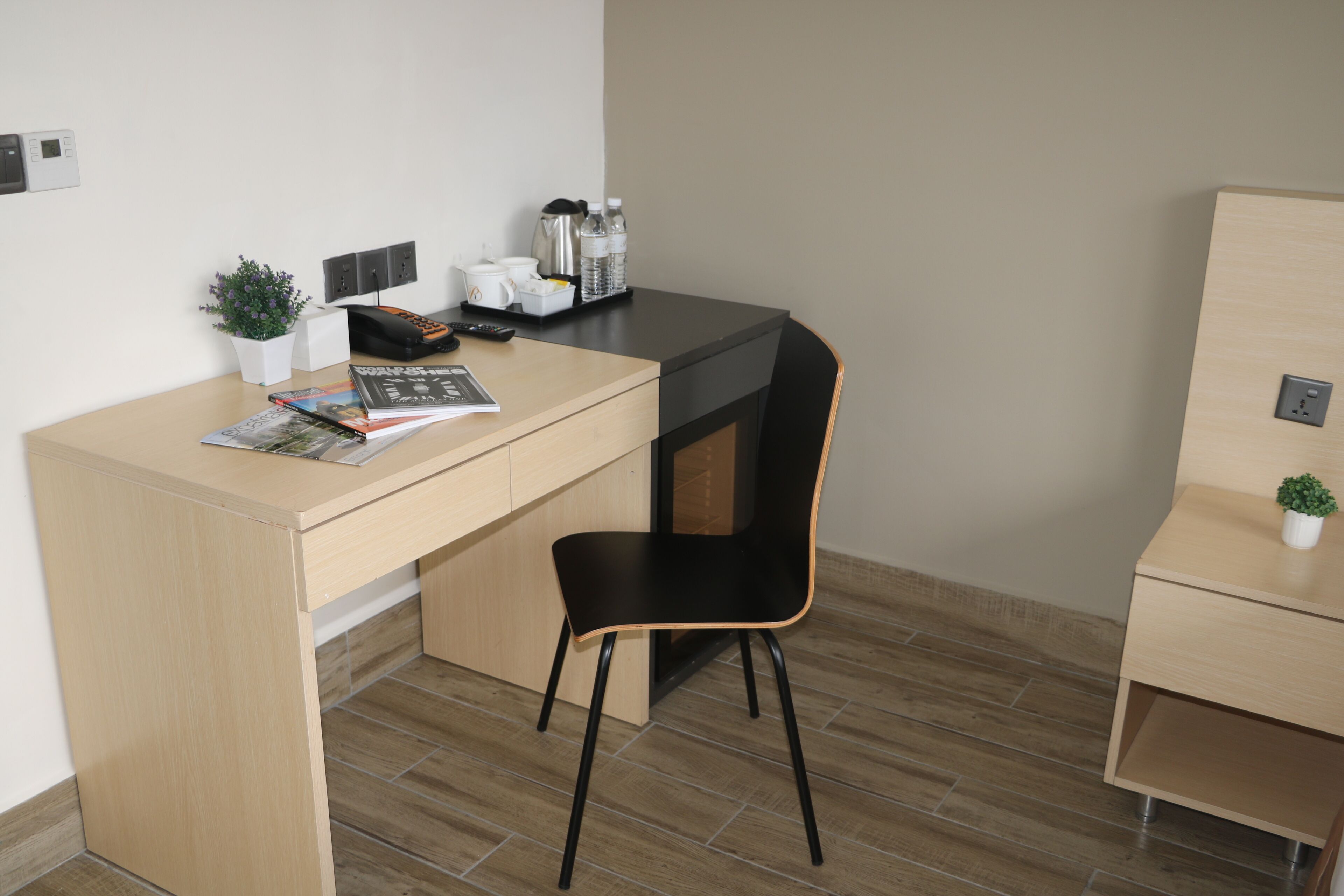 A small, modern office space with a wooden desk, a black chair, a potted plant, a coffee maker, and a water dispenser.