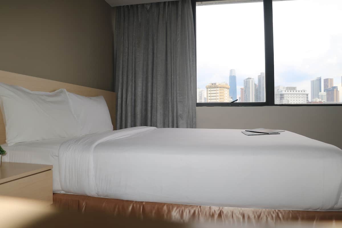 Habitación de hotel con una cama grande, una mesita de noche, un ventanal con vistas a la ciudad y una cortina.