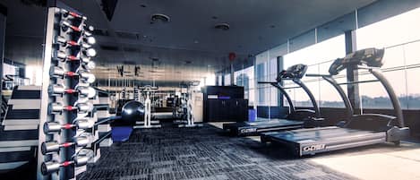 Un gimnasio con equipo de ejercicio, una cinta de correr Cybex y un soporte de mancuernas en la pared.