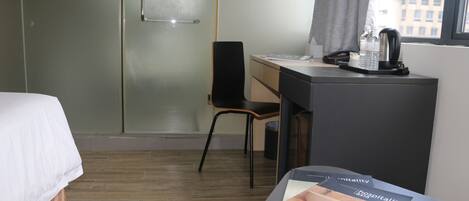 Una habitación de hotel con una cama, un escritorio, una silla, una mesita con una revista y una ventana que ofrece vistas a edificios.