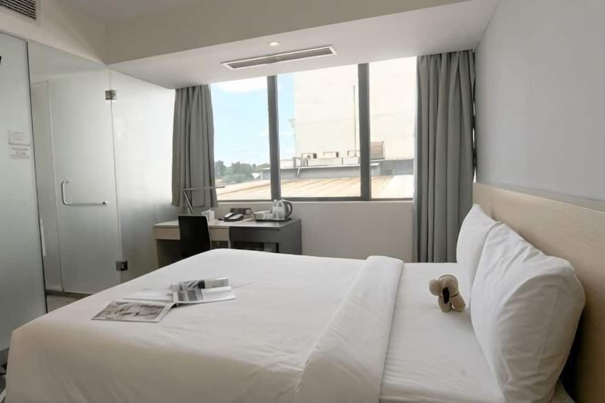 Habitación de hotel con cama, escritorio, silla, ventana con cortinas y vistas al exterior.
