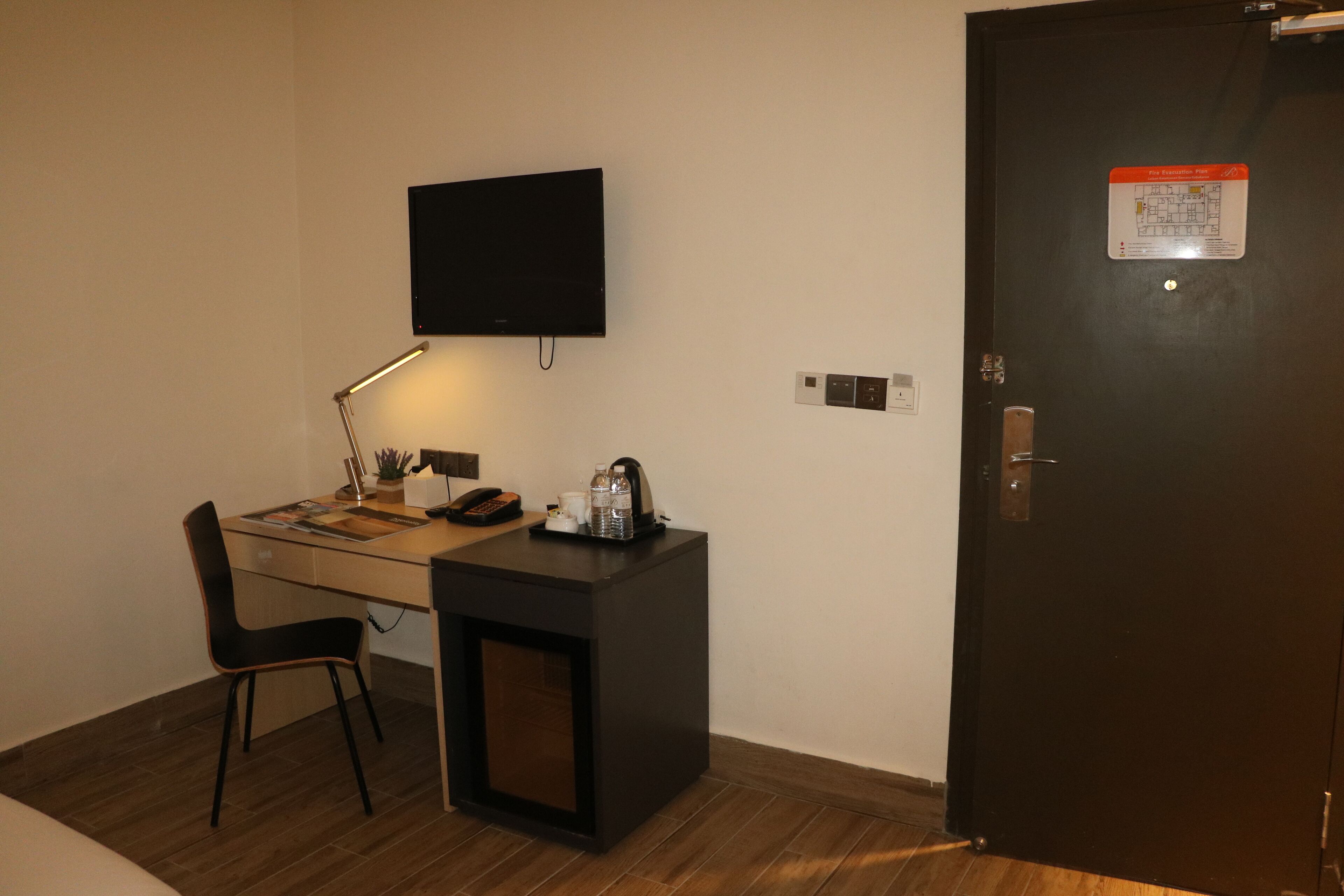 Una habitación pequeña y ordenada con un escritorio, una silla y un televisor de pantalla plana montado en la pared.