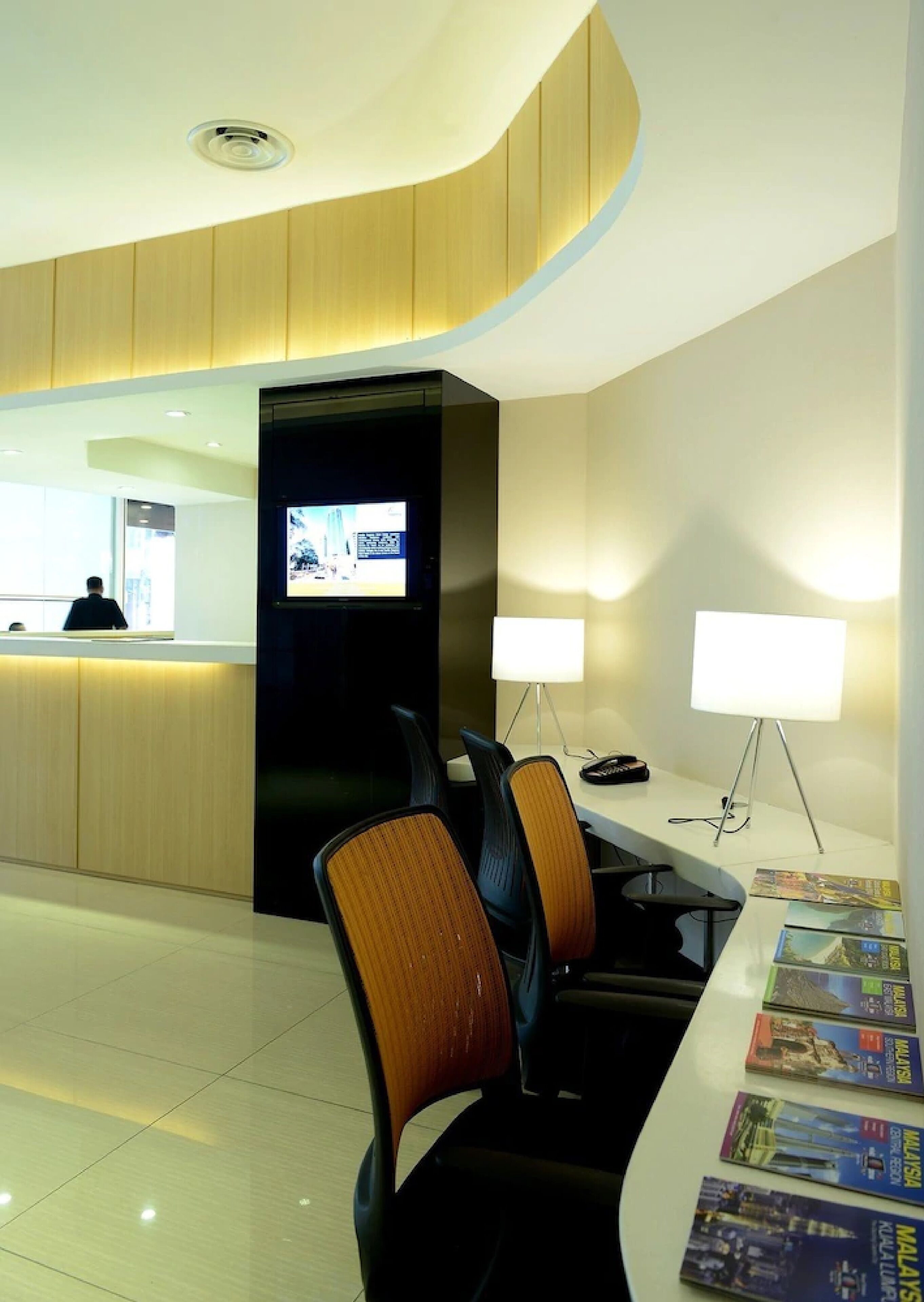 A modern hotel reception area with a curved ceiling, a reception desk, and a seating area with chairs and a table.