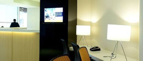 A modern hotel reception area with a curved ceiling, a reception desk, and a seating area with chairs and a table.