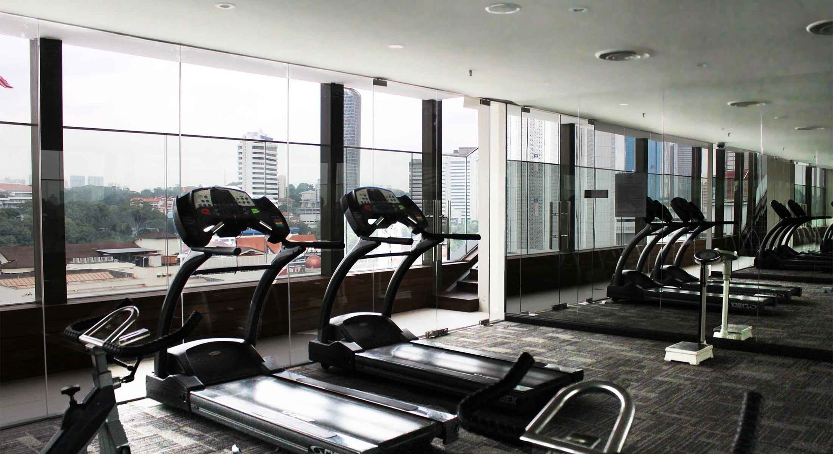A gym with treadmills and stationary bikes, large windows with a city view.