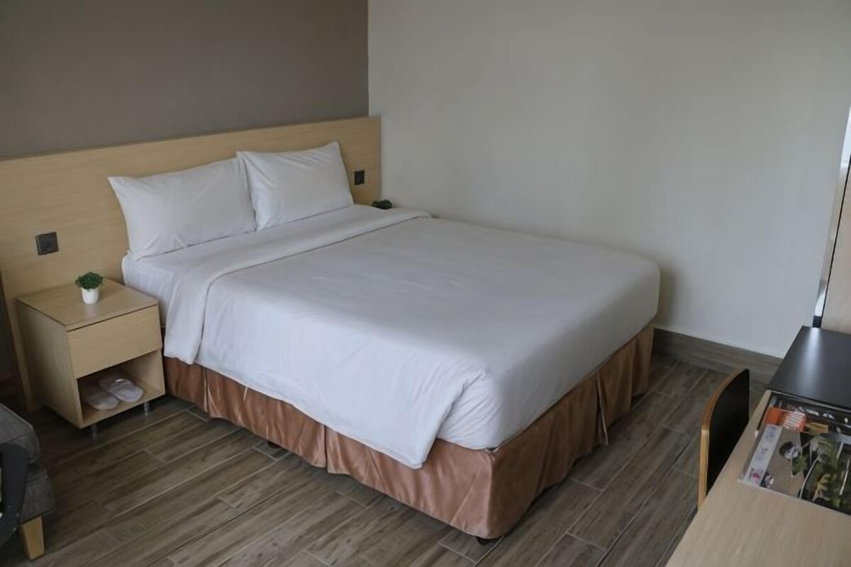 A neatly made bed with a wooden headboard, a bedside table with a lamp, and a small shelf with shoes.